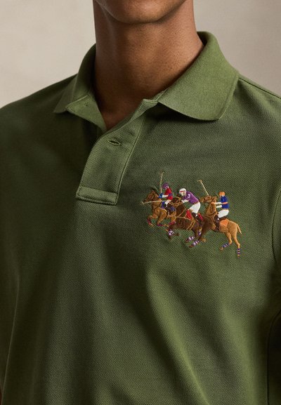 Άνδρας που φοράει πράσινο πουκάμισο πόλο με κεντητό σχέδιο τεσσάρων παίκτων πόλο που καβαλούν άλογα και κουνάνε μονόξυλα στο στήθος.
