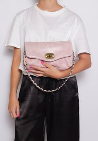 Borsa a mano in pelle rosa pallido con chiusura a pattina, hardware dorato e tracolla in catena metallica intrecciata. Presenta dettagli borchiati sui lati.