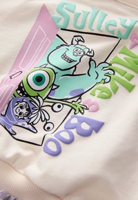 Sweat-shirt en coton avec illustration dessin animé de Sulley et Mike. Couleurs comprenant vert pastel, violet et rose. Comprend un design de texte ludique.