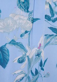 Tissu bleu clair avec un motif floral en blanc et nuances de teal, comprenant des pétales et des feuilles détaillés, texture lisse.