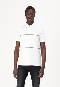 Hvid polo shirt med korte ærmer, der har to vandrette maroon striber. Lavet af tekstureret bomuld med krave og knaplister.