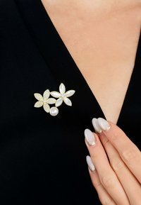 Gold-tone floral brooch with pearl accents, featuring two detailed flowers: one with clear rhinestones and the other with a polished surface.