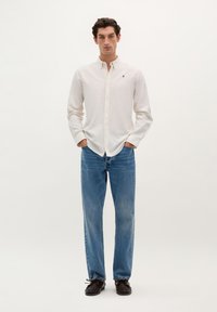 Hvidstribet klassisk skjorte med et brystlogo, parret med lyseblå lige ben jeans og brune sko. Simpelt design, afslappet look.