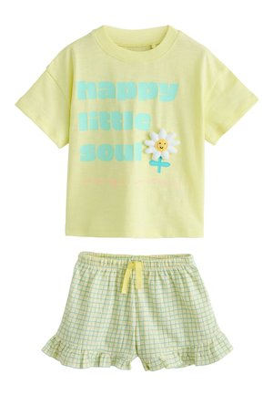 Gelbes Kurzarmhemd mit blauem "happy little soul"-Text und Gänseblümchen-Patch, kombiniert mit gelben karierten Shorts mit Rüschen am Saum und Kordelzug.
