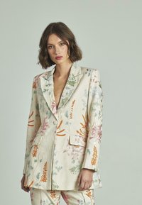 Blazer de lino bordado con patrones florales en colores pastel, con solapa en pico, cierre de doble botón y bolsillos delanteros.