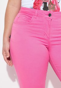 Vaaleanpunaiset farkut slim fit -mallissa, joissa on etutasku, vyölenkit ja napitus. Sileä pinta, jossa on hienovaraisia ompelutietoja.