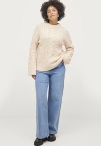 Maglione beige a maglia rasata con collo girocollo, polsini e orlo a coste, abbinato a jeans a gamba larga blu chiaro e stivaletti neri chunky.