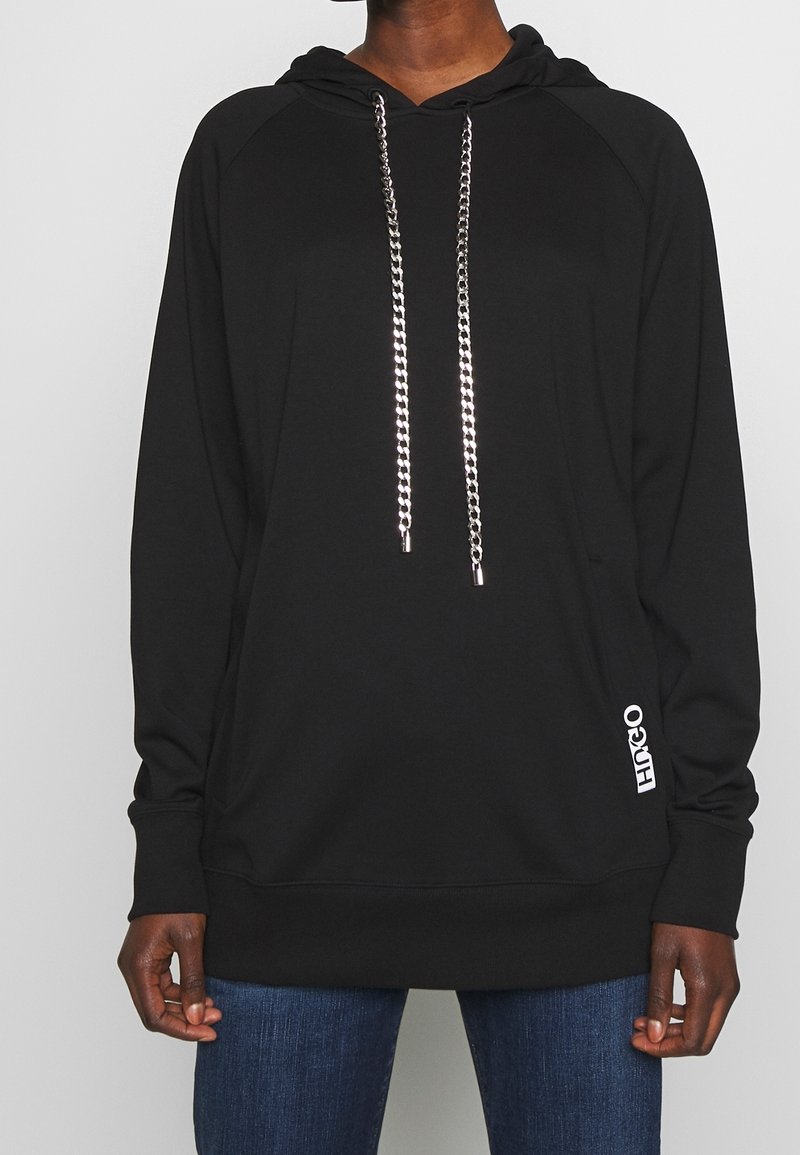 Sweat à capuche noir en tissu doux, avec une grande poche frontale, des cordons de serrage en chaîne argentée, et un accent de logo blanc sur le côté.