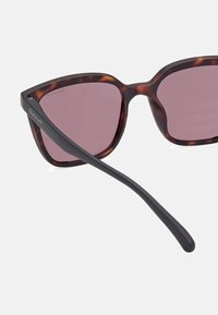 Ochelari de soare tortoise brown cu lentile roz și accente negre pe brațe, având un design elegant și geometric. Logo-ul GANT este vizibil.