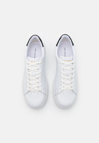 Baskets en cuir blanc à texture lisse, bout arrondi, lacets plats blancs et accent noir au talon. Nom de la marque visible à l'intérieur.