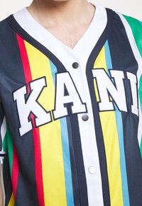 Korte mouw jersey met meerkleurige strepen (rood, geel, blauw, groen) met zwarte biezen en een witte knoopsluiting. Voorzijde met "KANI" in vetgedrukte letters.