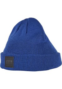 Plavi pleteni baret s prevrnutim rubom. Ima teksturirani rebrasti uzorak i crnu oznaku na rubu.