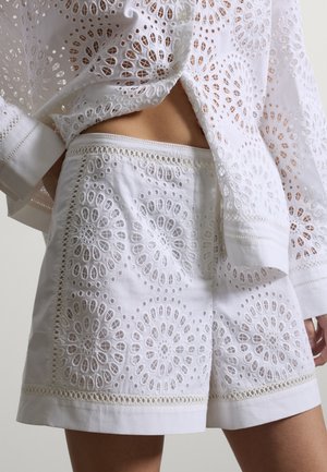 Weiße Baumwollshorts und passendes Oberteil mit runder Lochstickerei mit Blumenmustern, getragen von einer Person, die den Bauch zeigt.