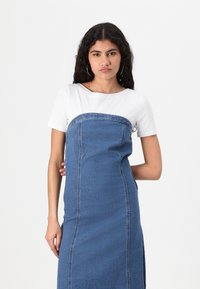 Jeans obleka s prilegajočim trupom in ravnim krilom, ki vključuje zgornji del s kratkimi rokavi v beli barvi, stranske šive in srebrne predstavitve. 