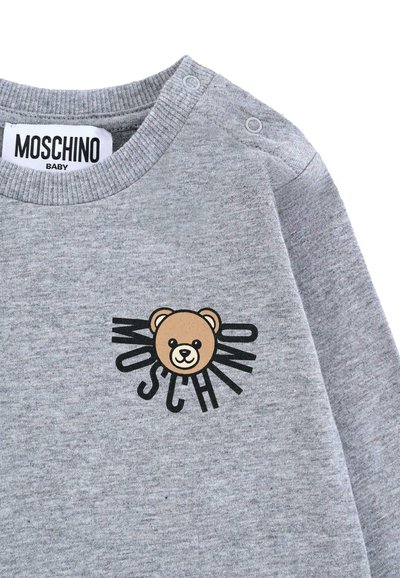 Felpa grigia con grafica di un orso e il testo nero "MOSCHINO" che si irradia da esso. Realizzata in tessuto morbido con scollo a giro e chiusure a scatto.
