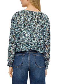 Bluse mit Blumenmuster aus transparenter Masse, mit langen Ärmeln und rundem Ausschnitt. Kombiniert mit dunkelblauen Jeans mit Gesäßtaschen.