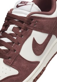 Sneakers Nike Dunk in pelle bianca e suede bordeaux, con tomaia testurizzata, chiusura con lacci e suola in gomma.