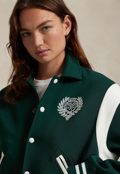 Zelena varsity jakna s bijelim prugama i gumbima, koja sadrži srebrni izvezeni logo i dizajn lovorovog vijenca na lijevoj strani prsnog koša.