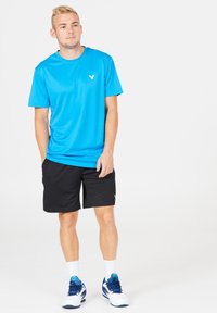 Ljusblå träningströja med korta ärmar, i kombination med svarta shorts. Har en liten logotyp på bröstet och vita träningsskor.