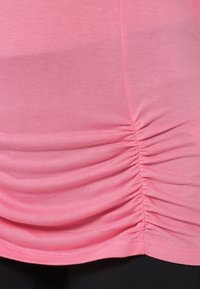 Różowy dopasowany top z marszczeniami po bokach i gładką teksturą. Linia dołu lekko zaokrąglona.