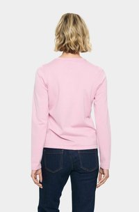 Pull rose à manches longues avec un col rond, texture lisse et design ajusté, associé à un jean en denim bleu foncé.
