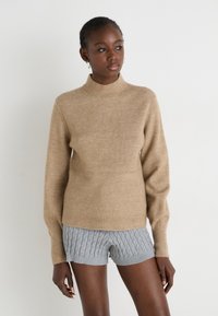 Tan ribbed sweater with a high neck and long sleeves, paired with gray textured shorts. Soft material, fitted design, and casual style.