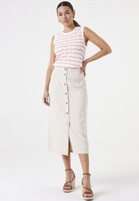 Haut sans manches avec des rayures ondulées roses, associé à une jupe en lin à taille haute avec boutons. Couleur claire, tissu texturé, et sandales à brides autour de la cheville.