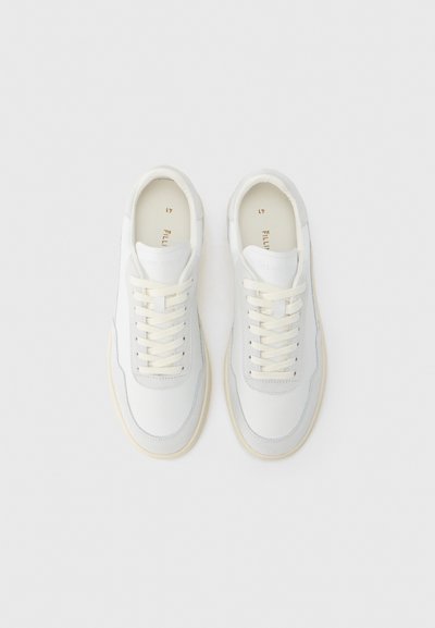 Λευκά δερμάτινα sneakers με λείο φινίρισμα, που διαθέτουν αντίθετες ανοιχτογκρι λεπτομέρειες, επίπεδα βαμβακερά κορδόνια και σόλα από καουτσούκ σε κρεμ απόχρωση.