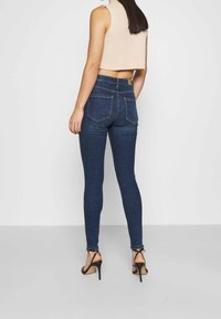 Mörkblå slim fit jeans med hög midja, med två bakfickor och en mjuk denimtextur. Stylad med svarta högklackade sandaler.