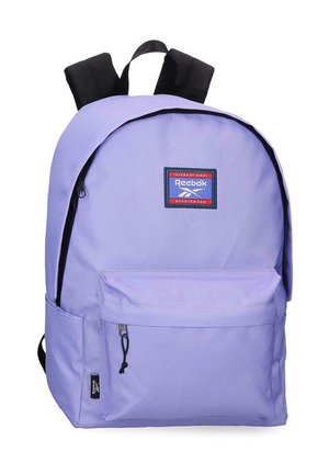 Mochila Reebok de color púrpura claro con correas acolchadas negras, bolsillo frontal con cremallera y parche con el logo de Reebok en la parte superior frontal.
