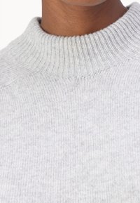 Pull léger gris, avec un col montant côtelé et un tricot doux et texturé. Vue en gros plan mettant en avant le tissu et les détails du col.