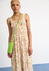 Bloemen maxi-jurk met lichtgroene en roze patronen, verstelbare bandjes en een geplooide taille. Vergezeld van een felgroene gehaakte tas.