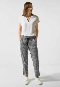 Witte, kortearmige top met V-hals, gecombineerd met grijs geruite broek met een elastische tailleband en zwarte trekkoord, aangevuld met witte sneakers.