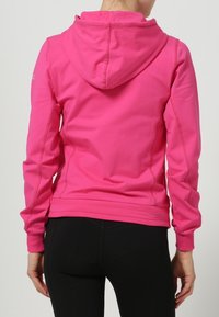 Vaaleanpunainen vetoketjullinen huppari, jossa huppu, valmistettu sileästä kankaasta. Siinä on tikattu yksityiskohtia ja istuva malli, yhdistetty mustiin leggingsseihin.