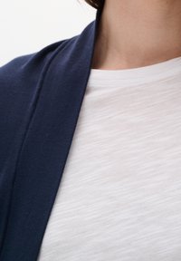 Cárdigan azul marino hecho de una tela suave con frente abierto, superpuesto sobre una camiseta blanca de manga corta con textura.