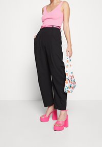 Débardeur rose côtelé, pantalon noir taille haute, sandales plateformes rose vif et sac fourre-tout à motif floral.