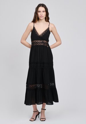 Vestido negro con escote en V profundo y detalles de encaje en la cintura y el dobladillo. Tela fluida con volantes en capas y tirantes finos ajustables.