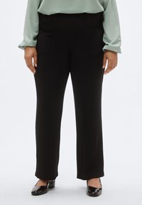 Μαύρο παντελόνι με ίσια γραμμή και δύο μπροστινές τσέπες. Το ύφασμα έχει ομαλή υφή. Συνδυάζεται με γυαλιστερά μαύρα παπούτσια.