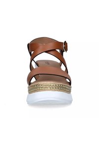 Sandali in pelle marrone con cinturini incrociati, suola piatta bianca e un'accattivante decorazione in oro intrecciato sul tacco. Chiusura con fibbia regolabile.