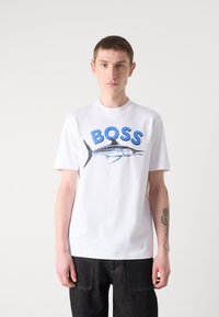 Camiseta de algodón blanca con texto azul "BOSS" y un gráfico de un pez marlín. Diseño de mangas cortas y cuello redondo.