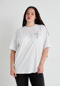 Bílý oversized tričko vyrobené z bavlny, s černým liniovým kresleným designem na levé straně hrudníku. Krátké rukávy a uvolněný střih.