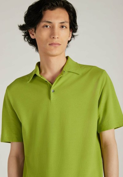 Camisa polo verde de manga corta hecha de tela suave, con un cuello clásico y una tapeta de un solo botón, con una textura suave y un corte relajado.
