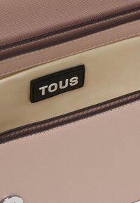 Interno della borsa rosa con texture, caratterizzato da una fodera beige e un'etichetta nera con testo bianco "TOUS". I bordi sono rifiniti con trim marrone.
