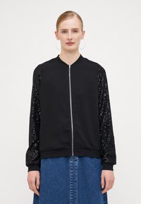 Black bomber jacket with a zip front; main body is smooth fabric, sleeves have textured black sequins. Ribbed cuffs complete the design.