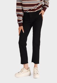 Jeans in denim neri con orlo sfrangiato, indossati con sneakers beige con piattaforma. L'outfit presenta un top a maniche lunghe a righe bordeaux e crema.