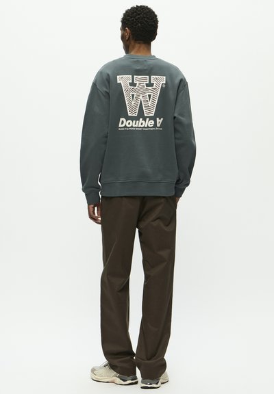 Sweatshirt charbon avec un grand graphique blanc du texte "W" et "Double A" au dos. Associé à un pantalon marron et des baskets neutres.