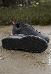 Black athletic shoes with a textured upper, gray accents, and red details; rugged outsole with prominent traction lugs for grip.