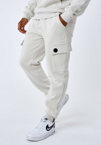 Pantalones cargo de color beige claro, hechos de una tela suave, con dos bolsillos laterales, un detalle de botón en la solapa del bolsillo y puños ajustados.