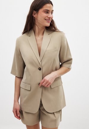 Bežový sako s krátkym rukávom, s klopami, jedným gombíkom, dvoma prednými vreckami a hladkou textúrou látky, doplnené o zodpovedajúce kraťasy.