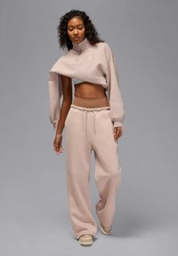 Lichtroze cropped sweatshirt met een hoge kraag, gecombineerd met wijde sweatpants in dezelfde kleur, voorzien van een taille met trekkoord.